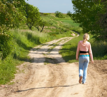teenage girl in low-cut jeans walking down dirt road